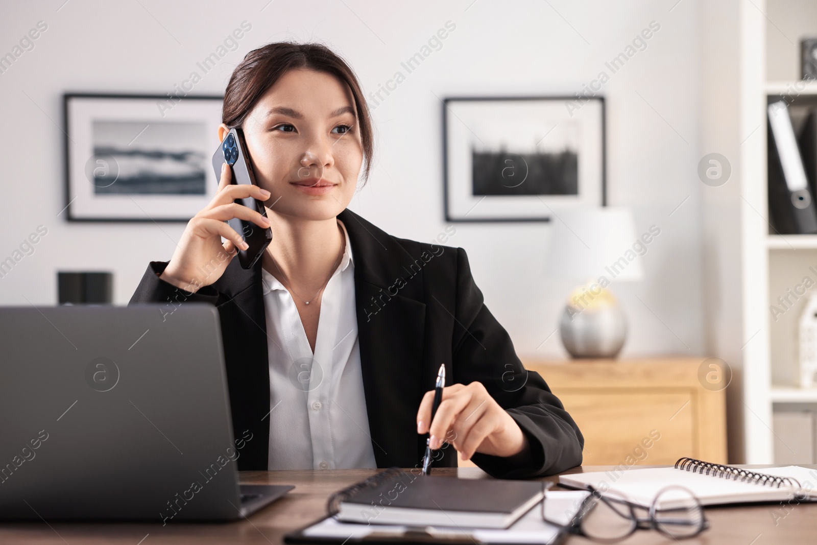 Photo of Beautiful businesswoman talking on smartphone at table in office