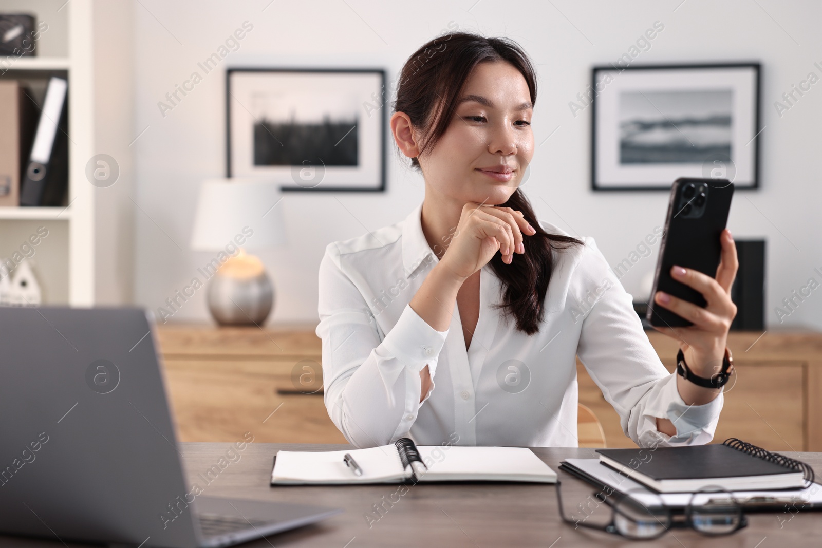 Photo of Beautiful businesswoman with smartphone at table in office