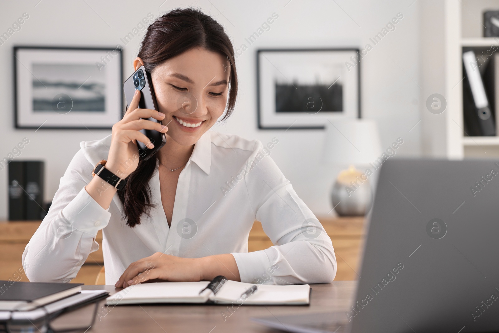 Photo of Smiling businesswoman talking on smartphone at table in office