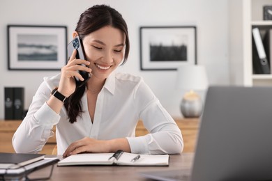 Smiling businesswoman talking on smartphone at table in office