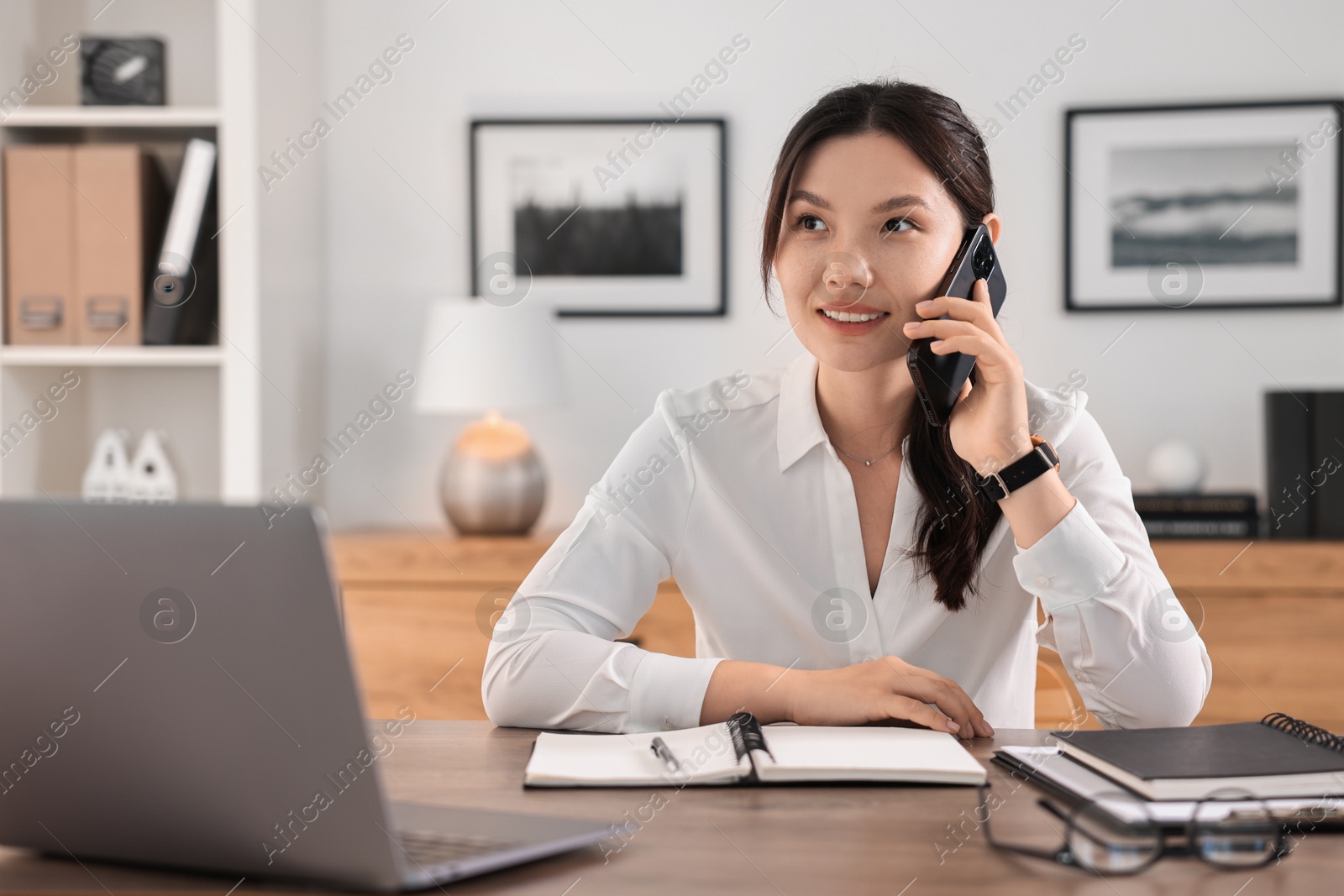 Photo of Smiling businesswoman talking on smartphone at table in office