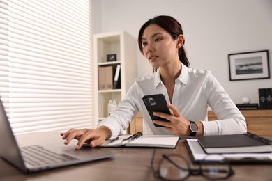 Photo of Beautiful businesswoman with smartphone working at table in office, low angle view