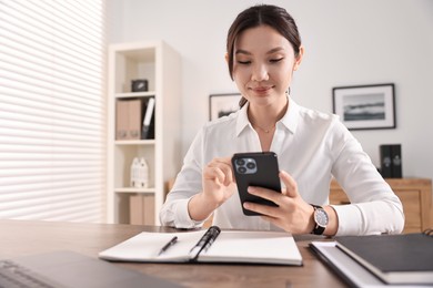 Photo of Beautiful businesswoman with smartphone at table in office