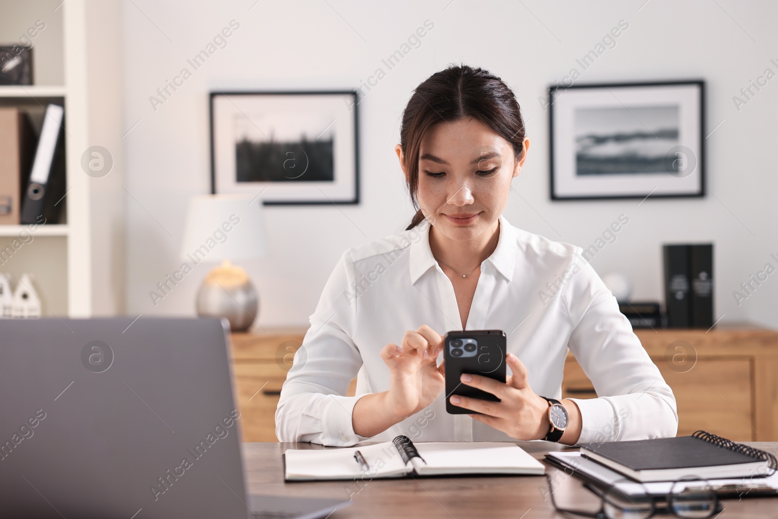 Photo of Beautiful businesswoman with smartphone at table in office