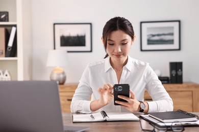 Beautiful businesswoman with smartphone at table in office