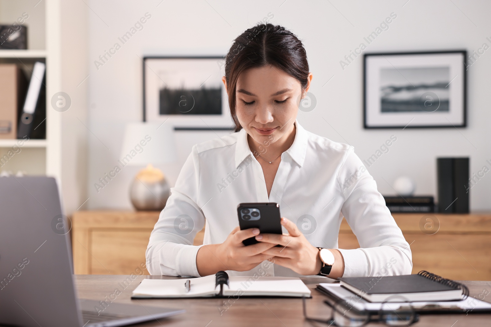 Photo of Beautiful businesswoman with smartphone at table in office