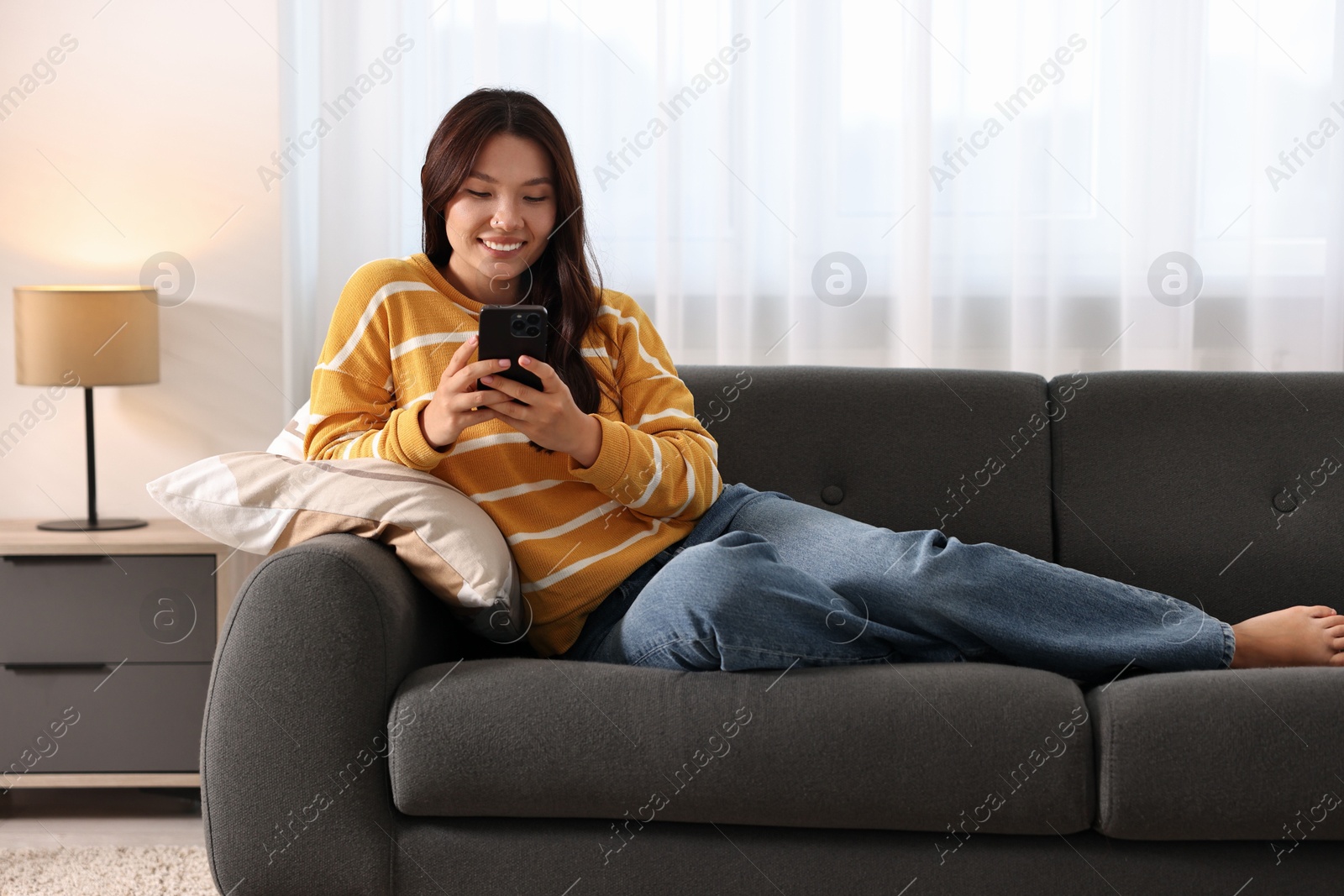 Photo of Smiling woman with smartphone on sofa at home