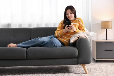 Photo of Smiling woman with smartphone on sofa at home