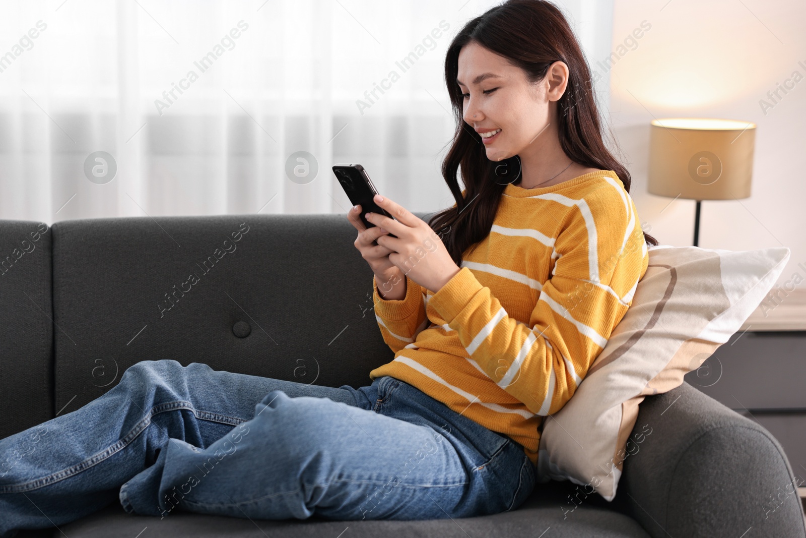 Photo of Smiling woman with smartphone on sofa at home