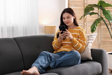 Photo of Beautiful young woman using smartphone at home