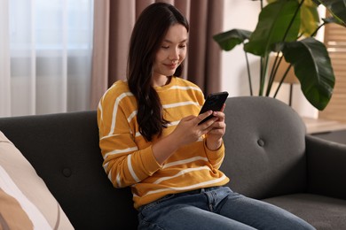 Photo of Beautiful young woman using smartphone at home