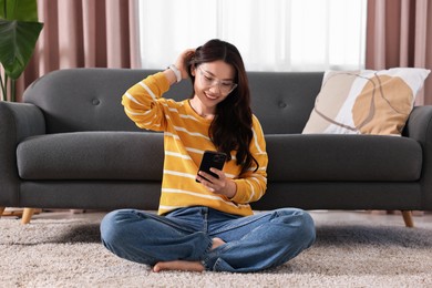 Photo of Smiling woman with smartphone sitting on carpet at home