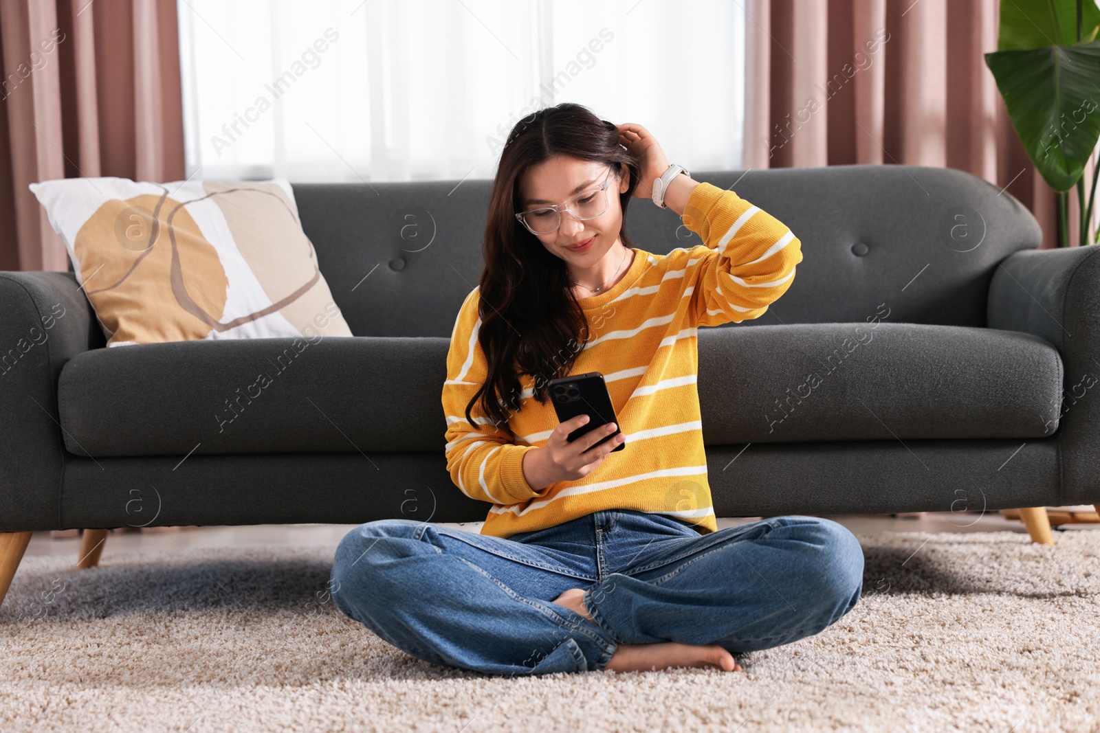 Photo of Beautiful woman with smartphone sitting on carpet at home