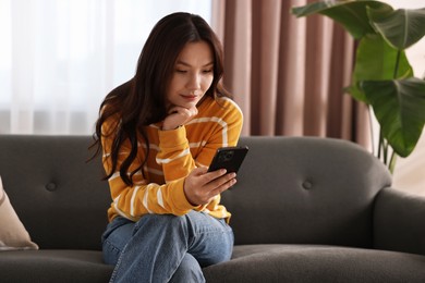 Photo of Beautiful woman using smartphone on sofa at home