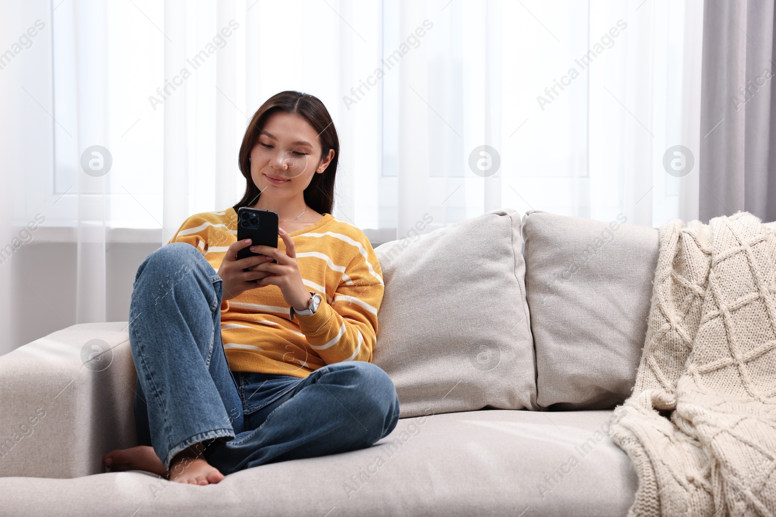 Photo of Beautiful woman using smartphone on sofa at home