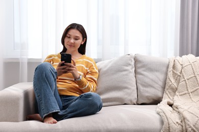 Beautiful woman using smartphone on sofa at home