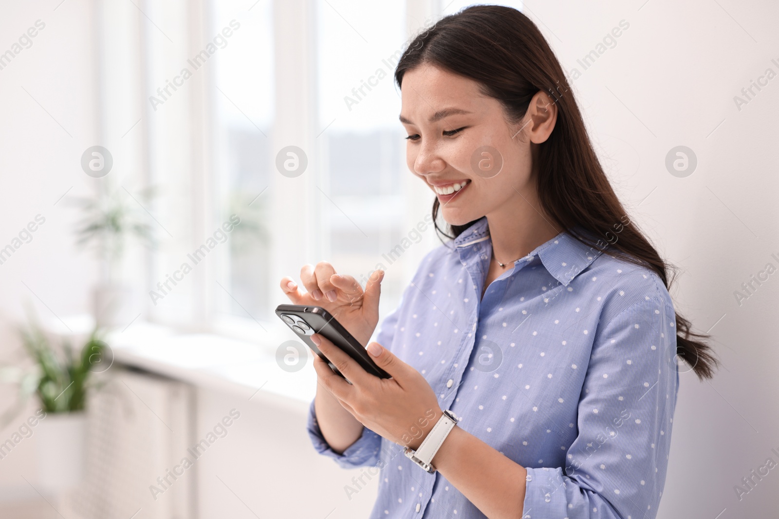 Photo of Smiling businesswoman using smartphone in office. Space for text