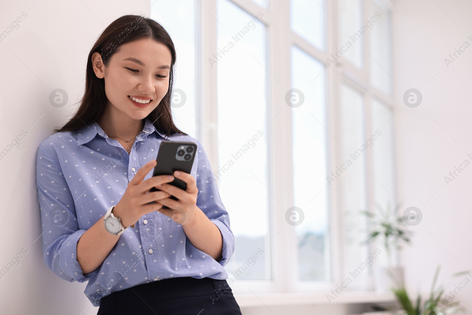 Photo of Smiling businesswoman using smartphone in office. Space for text