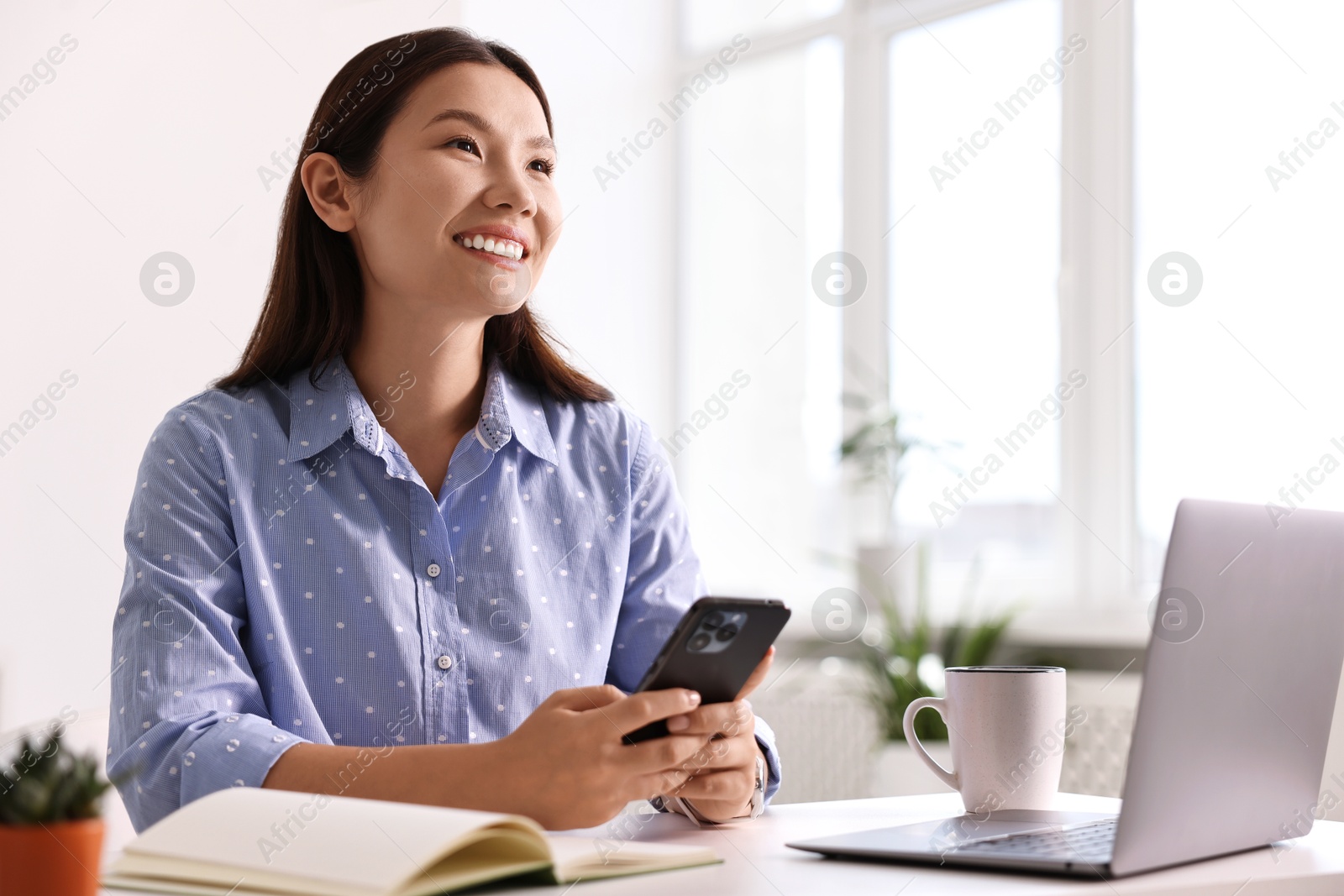 Photo of Smiling businesswoman with smartphone at table in office