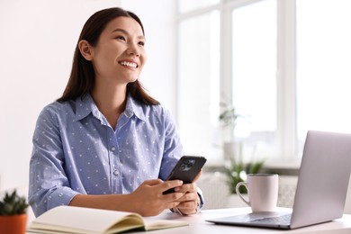 Photo of Smiling businesswoman with smartphone at table in office