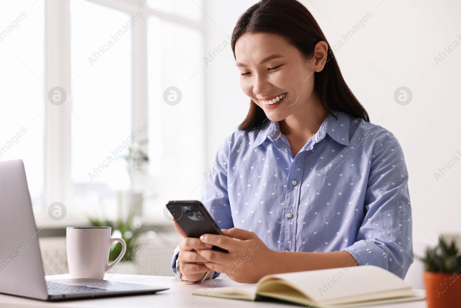 Photo of Smiling businesswoman with smartphone at table in office