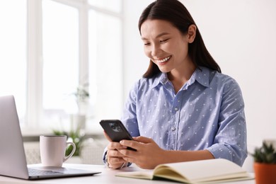 Smiling businesswoman with smartphone at table in office