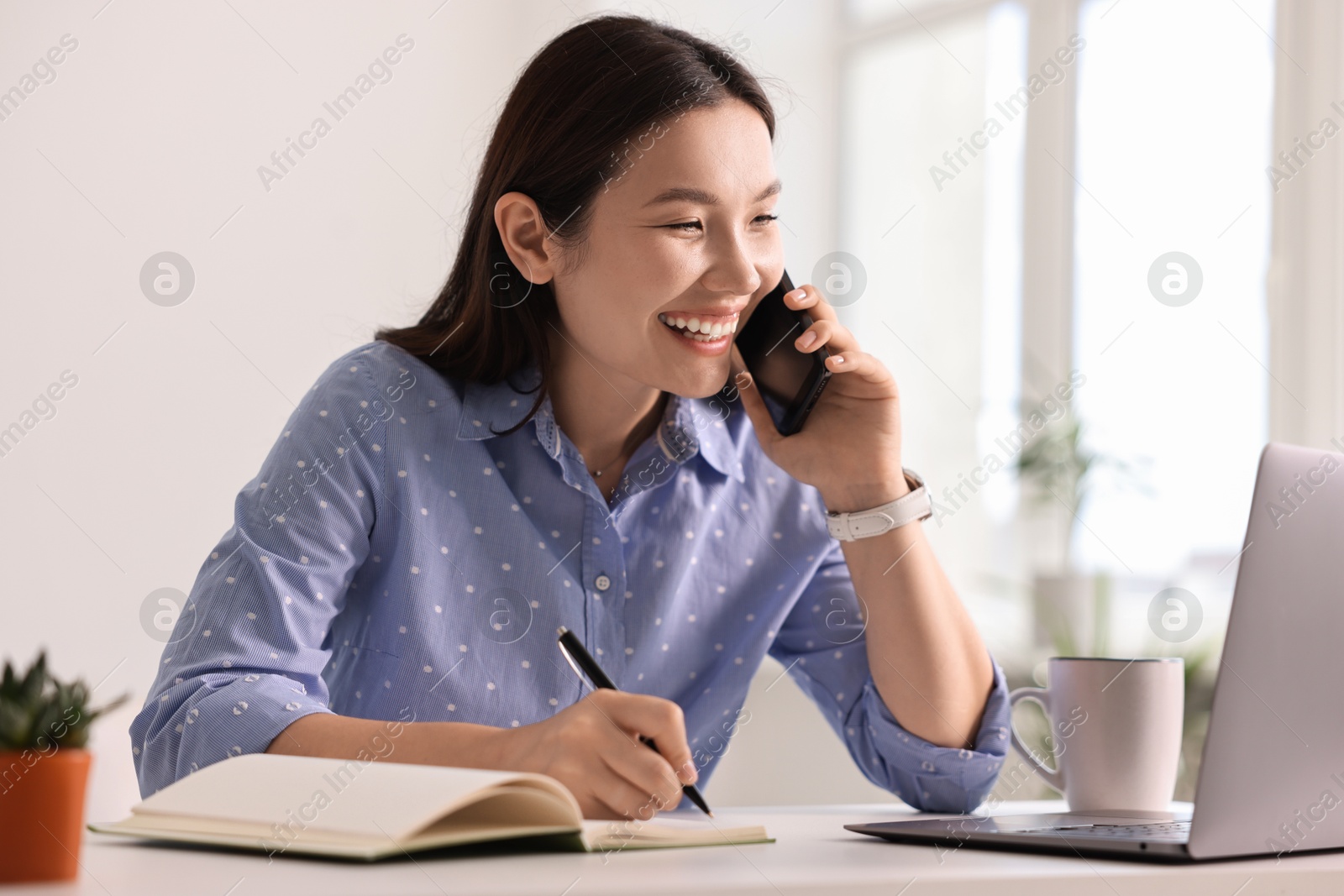 Photo of Smiling businesswoman talking on smartphone at table in office