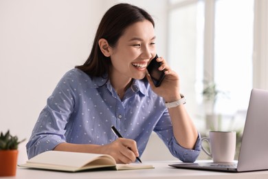 Photo of Smiling businesswoman talking on smartphone at table in office