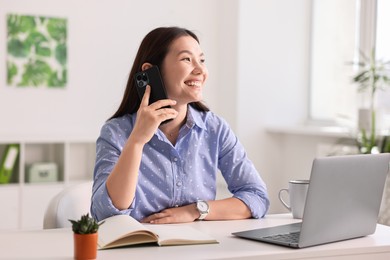 Photo of Smiling businesswoman talking on smartphone at table in office