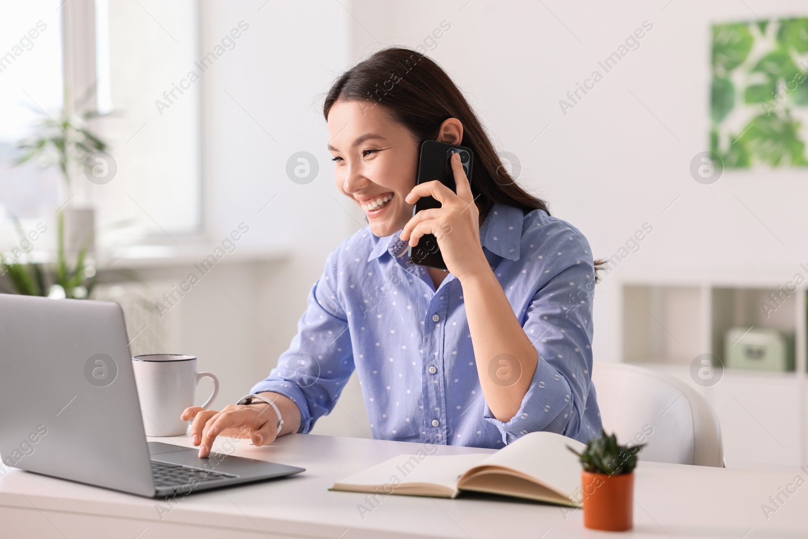 Photo of Smiling businesswoman talking on smartphone at table in office