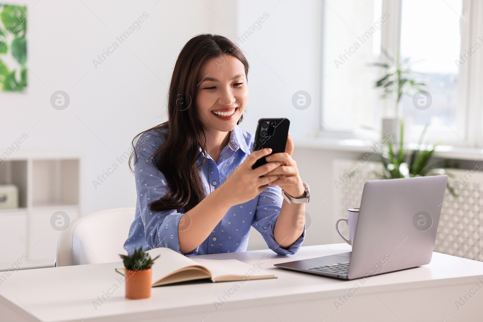 Photo of Smiling businesswoman with smartphone at table in office