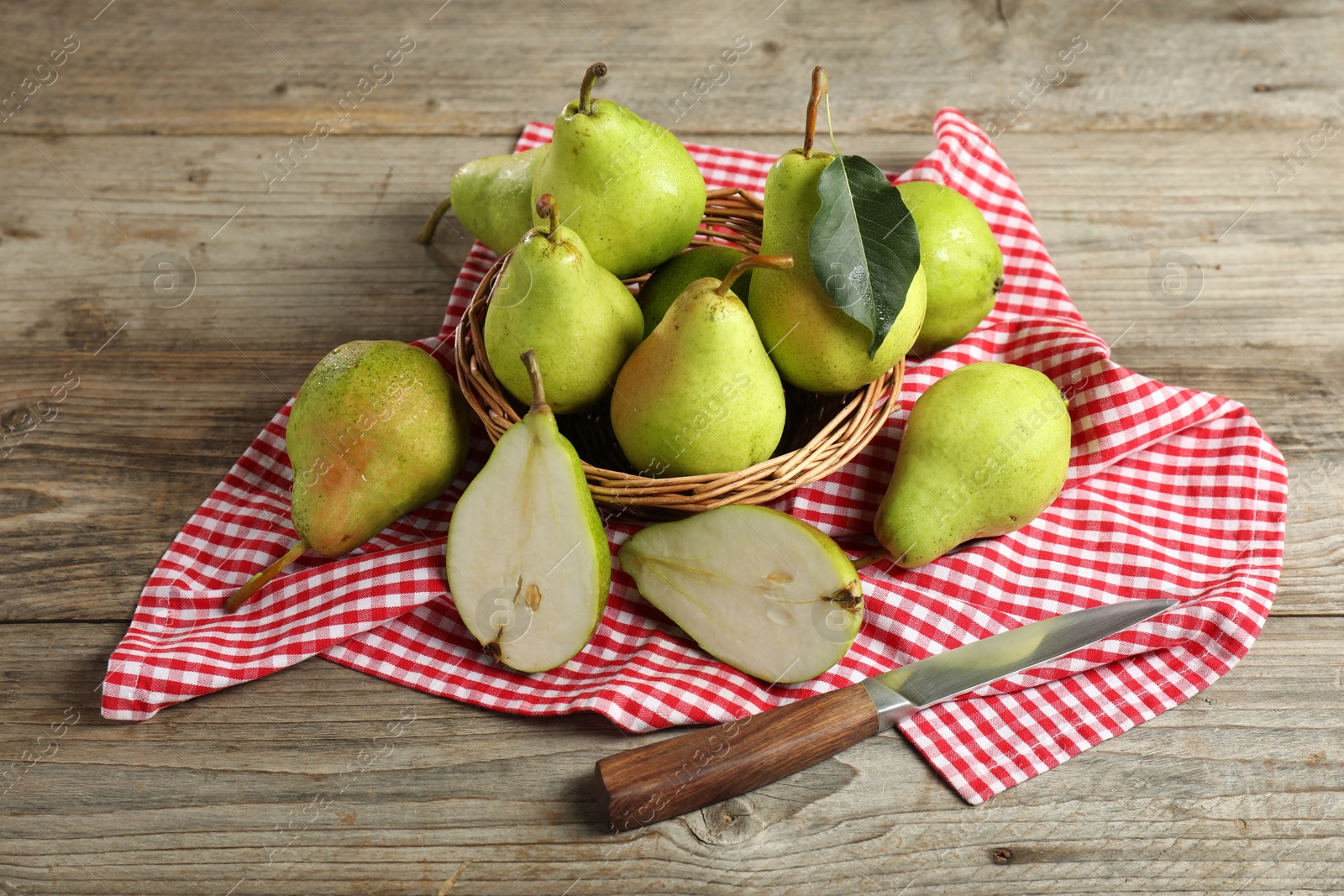 Photo of Fresh green pears, wicker basket, knife and napkin on wooden table