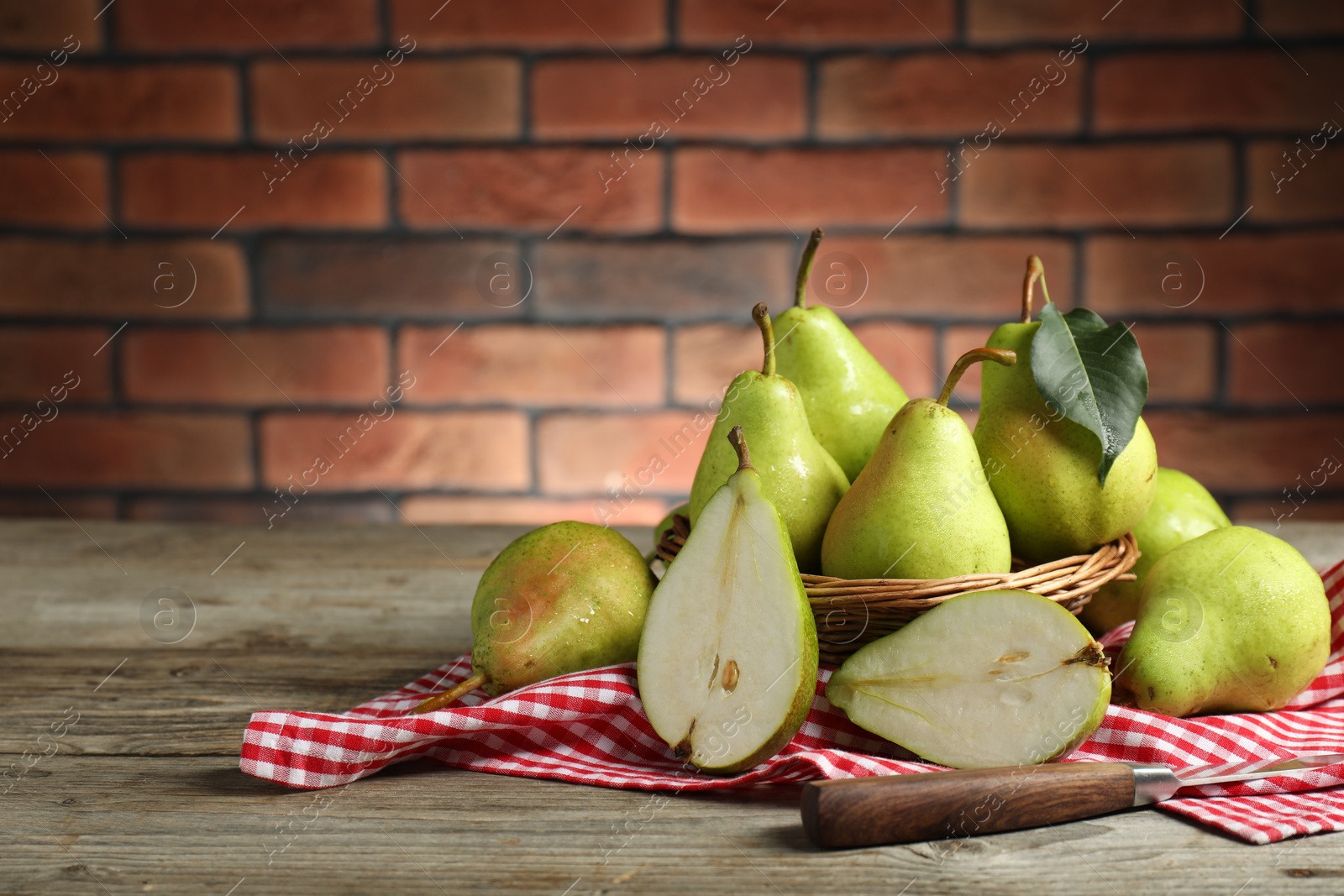 Photo of Fresh green pears and knife on wooden table against brick wall. Space for text