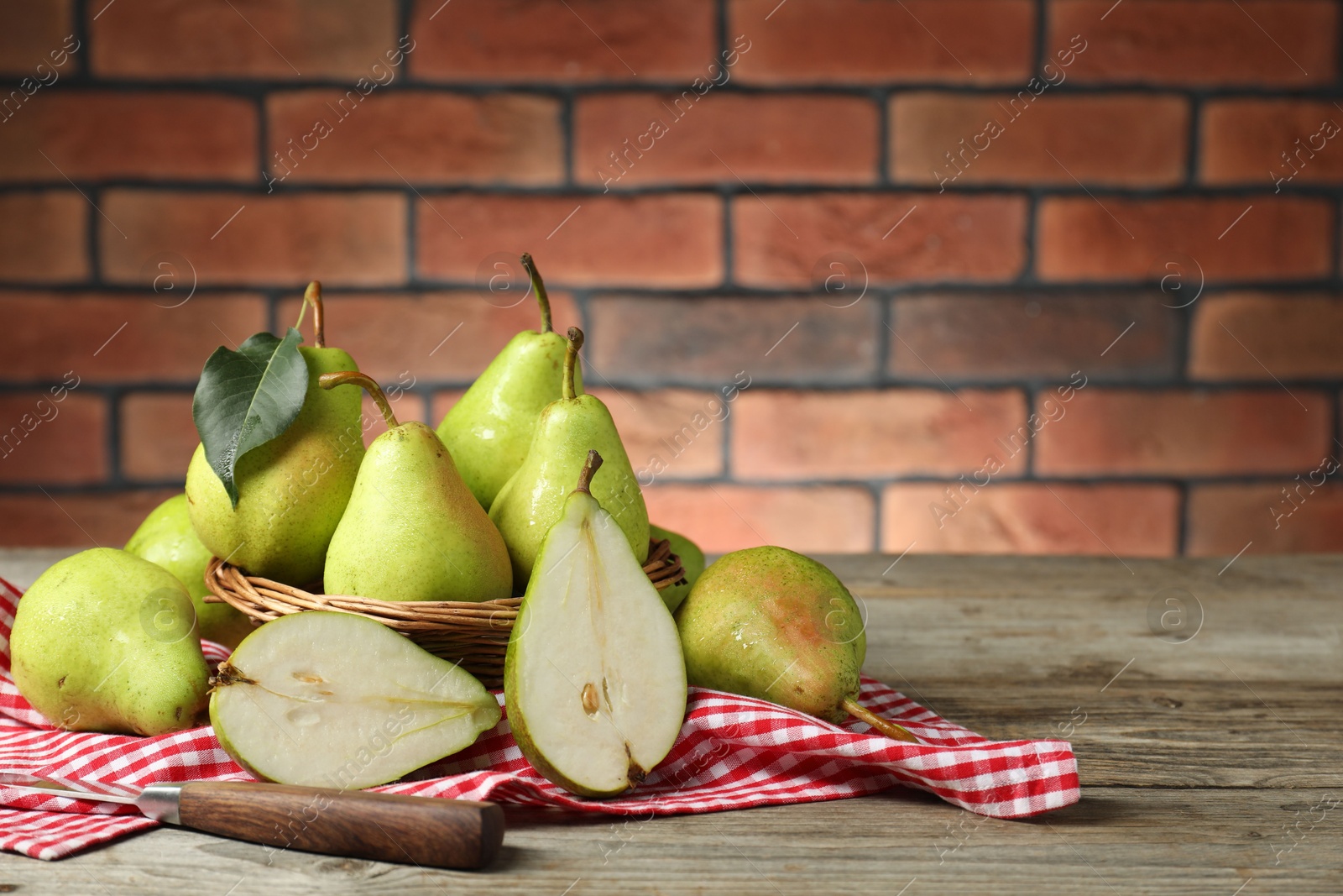 Photo of Fresh green pears and knife on wooden table against brick wall. Space for text