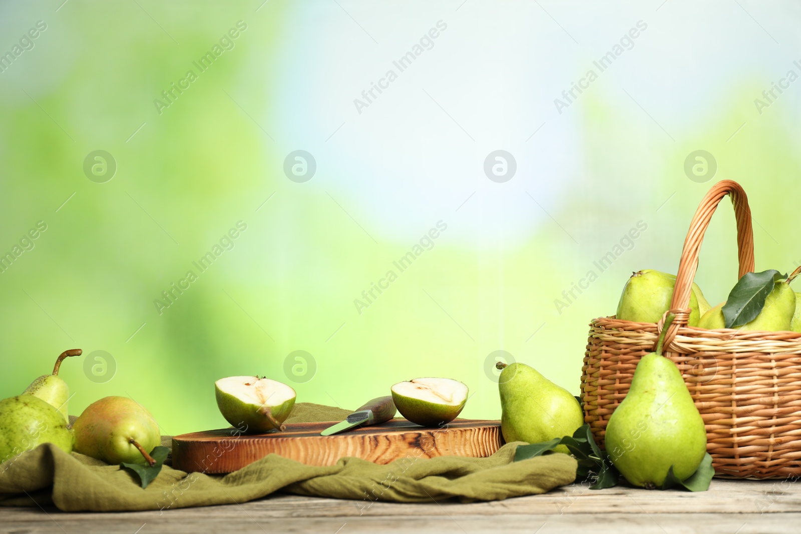 Photo of Fresh pears, knife and napkin on wooden table against blurred green background. Space for text