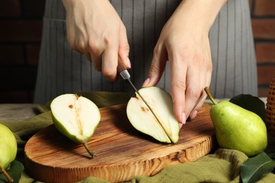 Photo of Woman cutting fresh green pears at wooden table, closeup