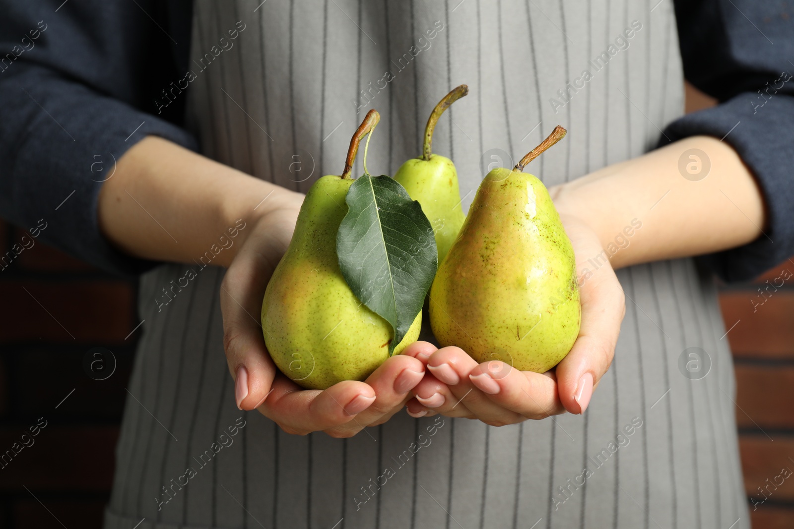 Photo of Woman holding fresh pears with leaf against brick wall, closeup