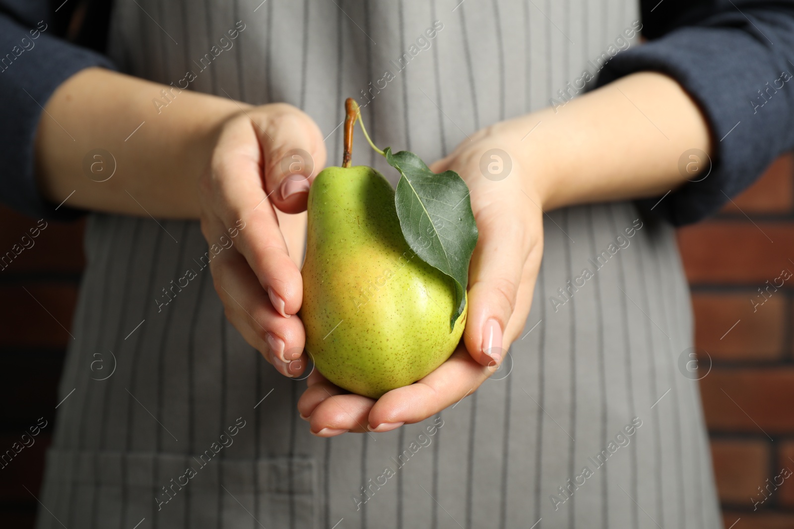 Photo of Woman holding fresh pears with leaf against brick wall, closeup