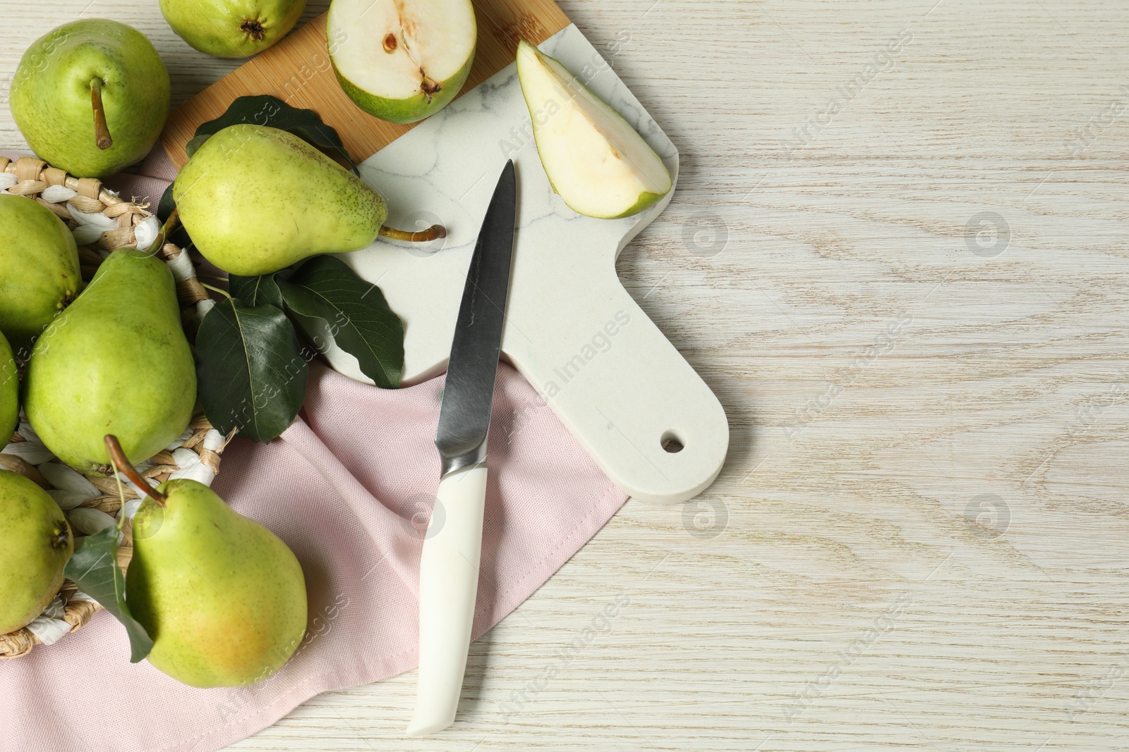 Photo of Fresh green pears with leaves and knife on light wooden table. Space for text