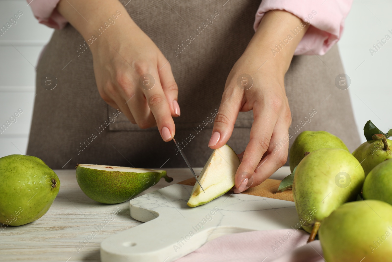 Photo of Woman cutting fresh green pears at light wooden table, closeup