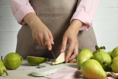 Photo of Woman cutting fresh green pears at light wooden table, closeup