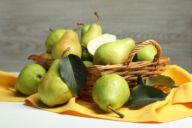 Photo of Fresh green pears with leaves and basket on white table, closeup