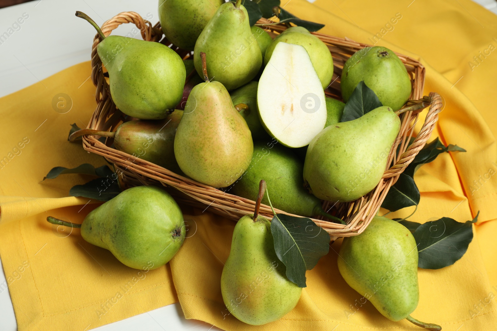 Photo of Fresh green pears with leaves and basket on white table, above view