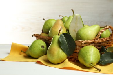 Photo of Fresh green pears with leaves and basket on white table, closeup