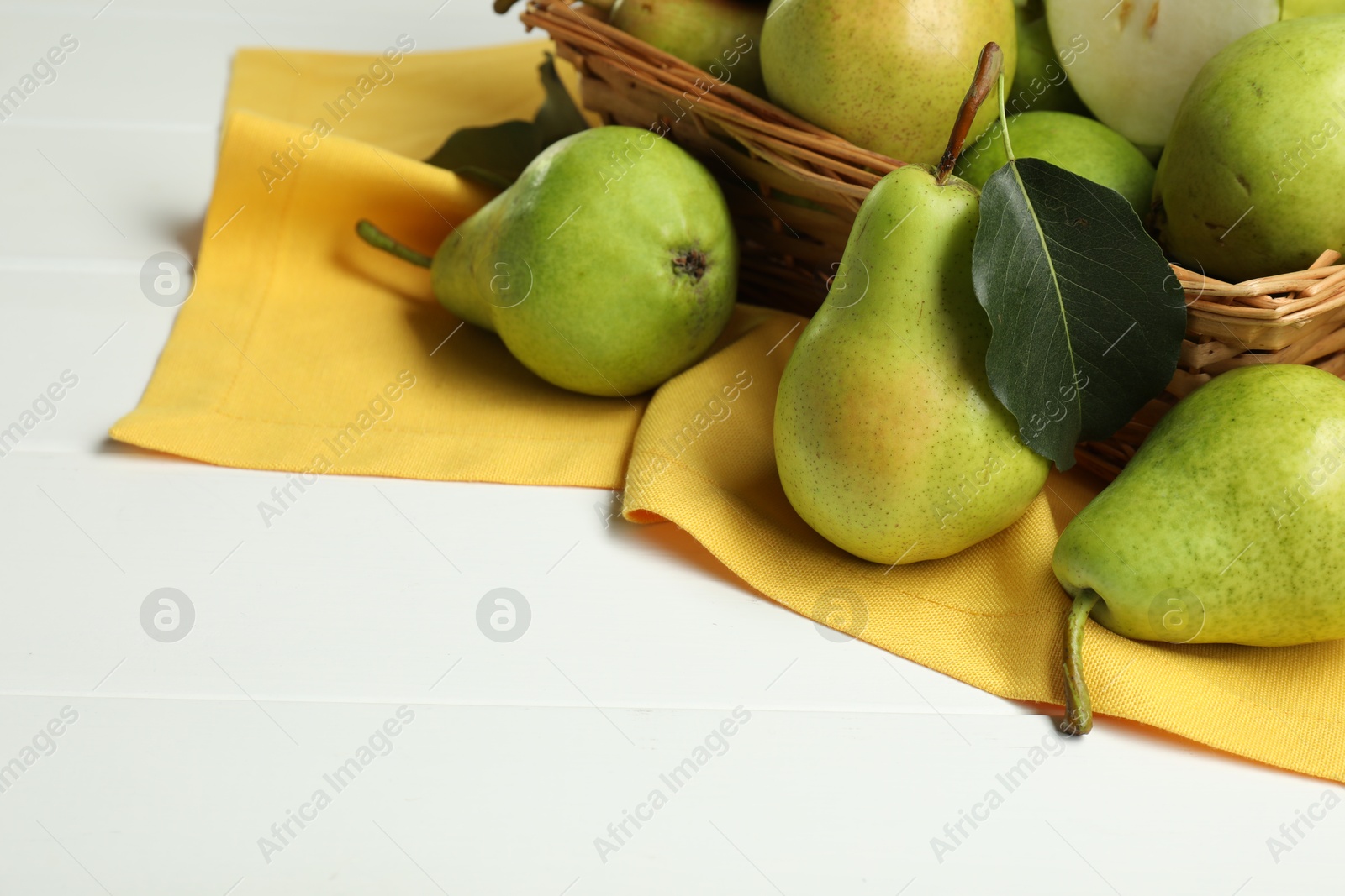 Photo of Fresh green pears and basket on white table, closeup