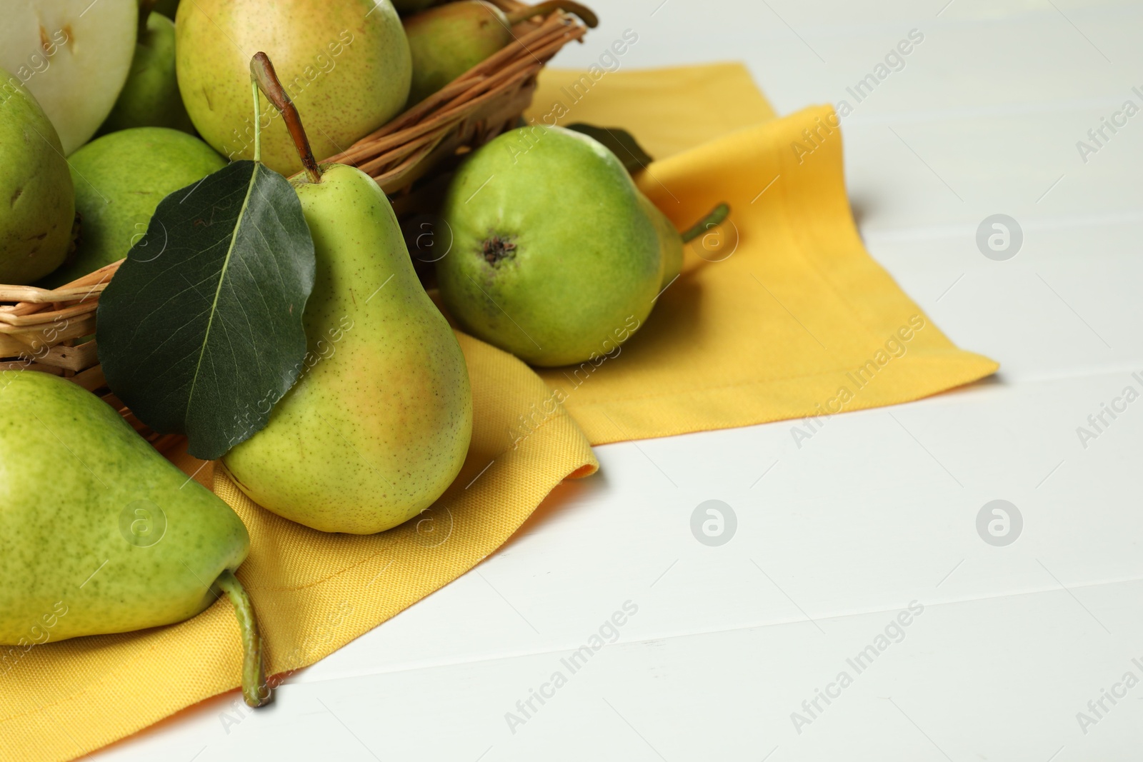 Photo of Fresh green pears and basket on white table, closeup