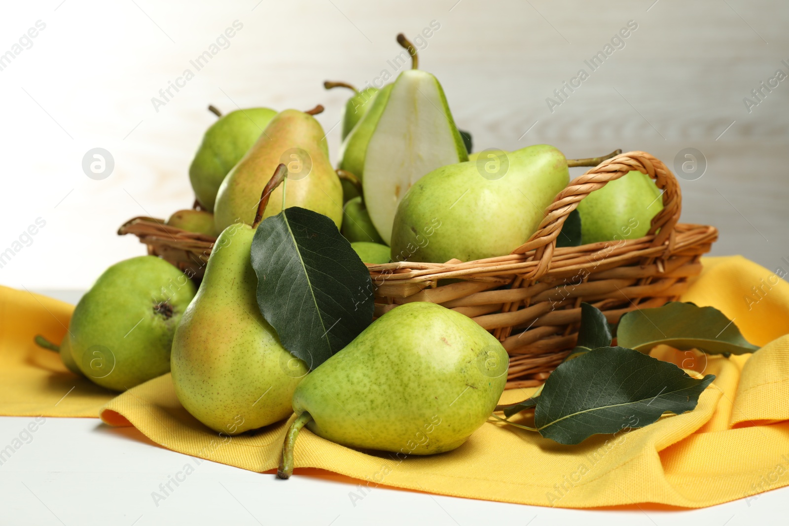 Photo of Fresh green pears with leaves and basket on white table, closeup