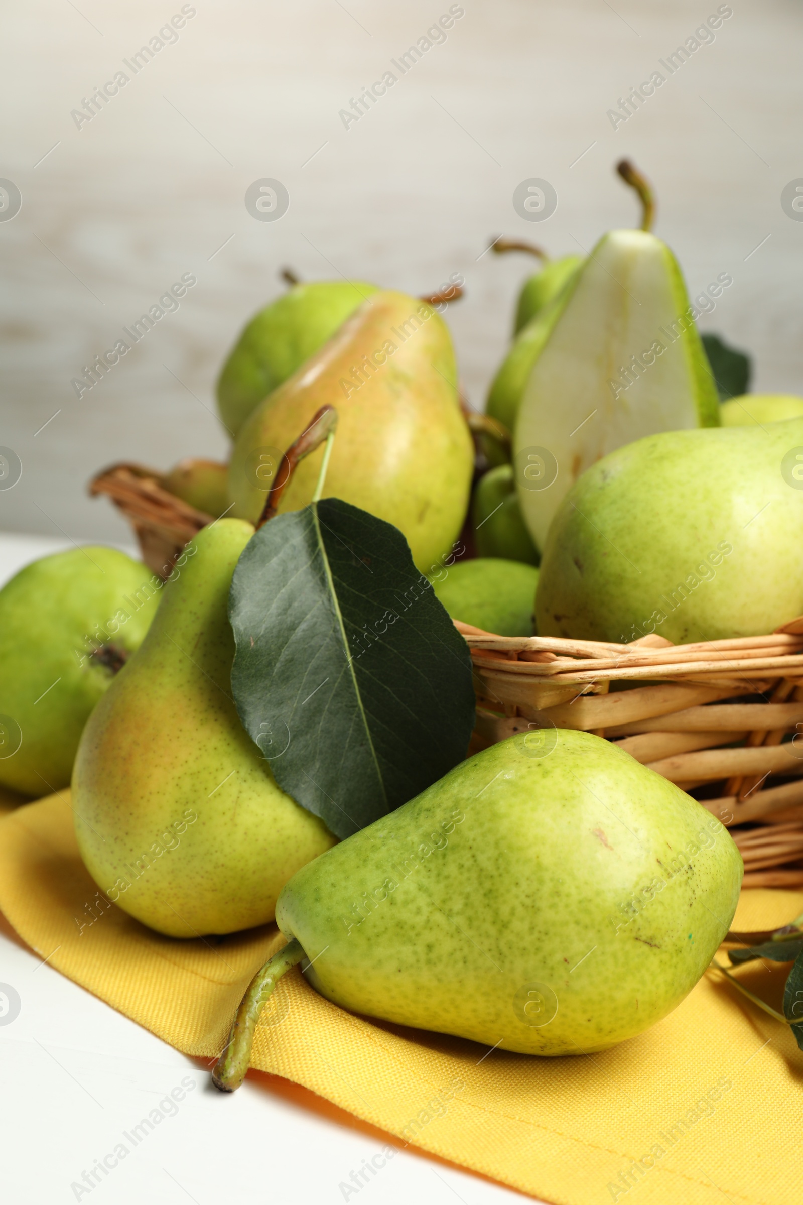 Photo of Fresh green pears with leaves and basket on white table, closeup