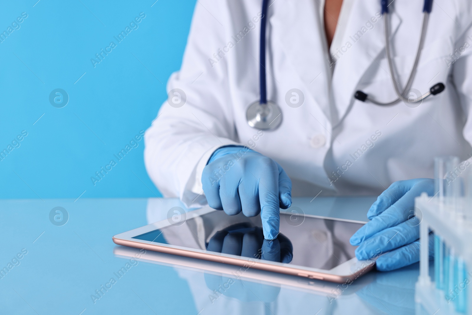 Photo of Doctor with tablet at table against light blue background, closeup view