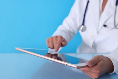 Photo of Doctor with tablet at table against light blue background, closeup view